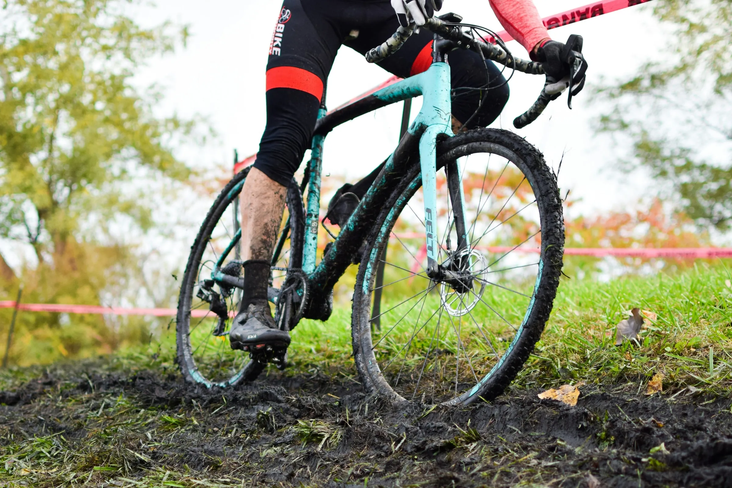 De benen van een veldrijder, onder de modder, op de pedalen