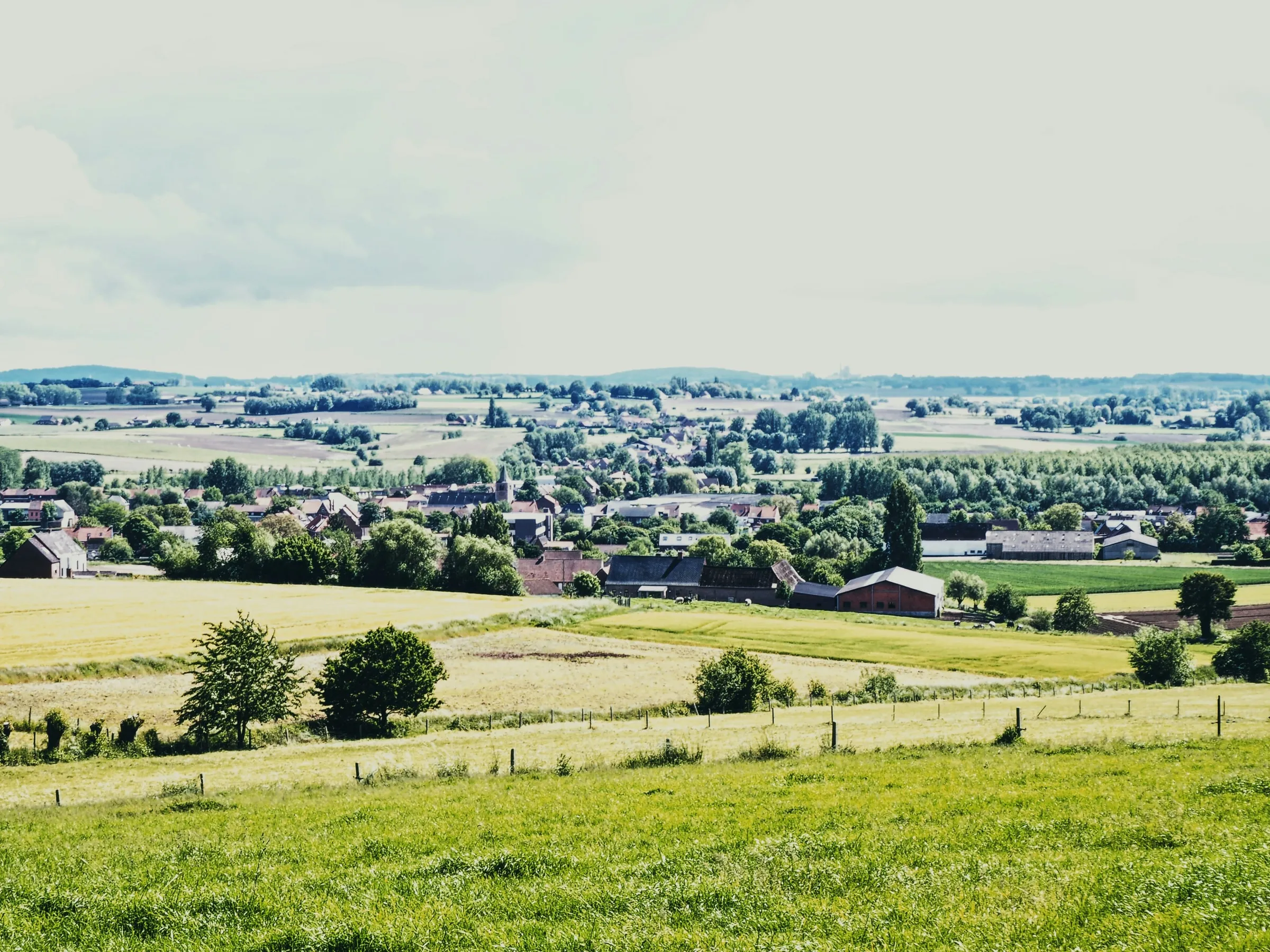 Glooiende weiden, een dorp met een kerk en heuvels in de verte